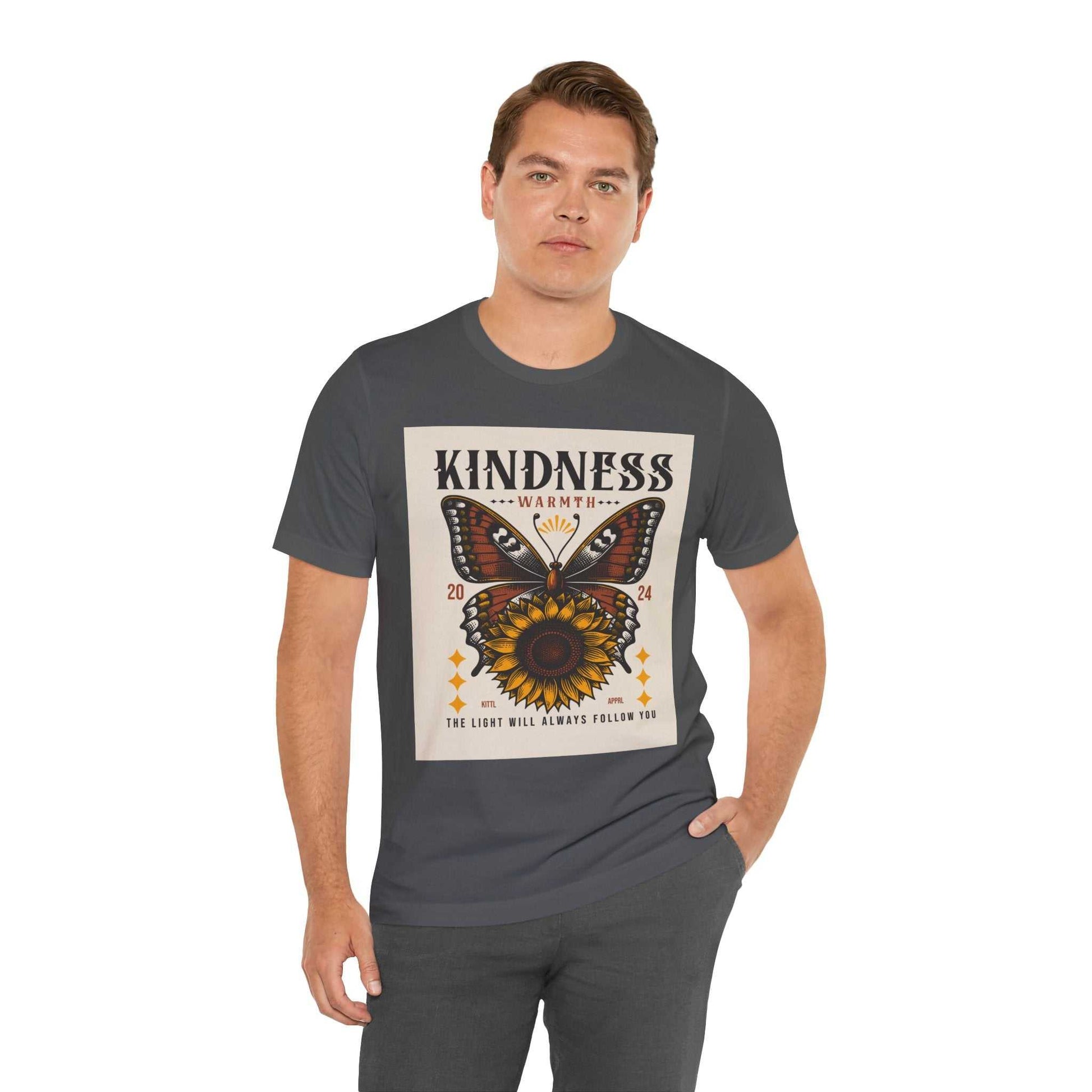 Man wearing a dark gray Kindness Butterfly Tee with a butterfly and sunflower graphic and the text "Kindness Warmth 2024 The light will always follow you"