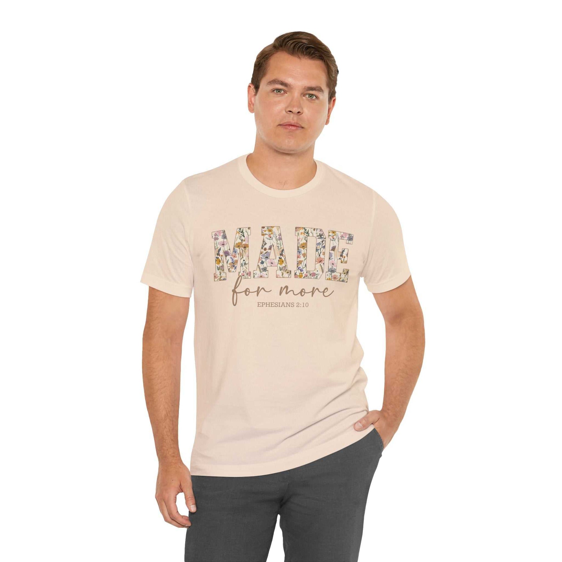 Man wearing a beige Made for More Tee with floral print text and black pants.