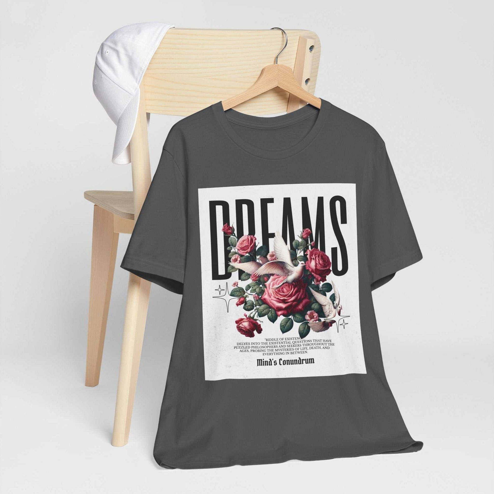 Dark grey Dreams Floral Tee with bold typography and red rose graphic on front displayed on wooden chair with white cap hanging on backrest