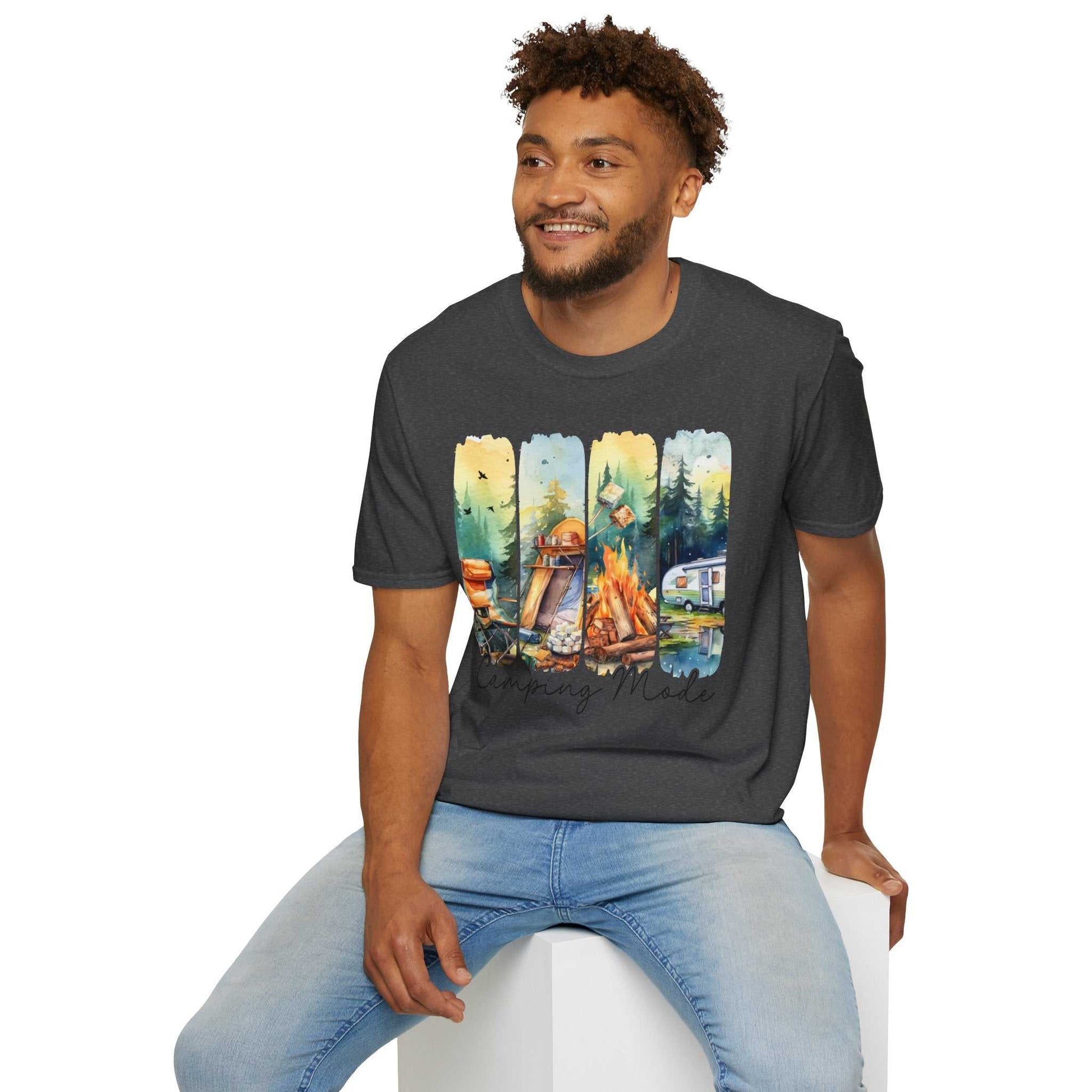Man wearing a dark gray Camping Adventure Unisex T-Shirt with colorful camping-themed graphics sitting on a white cube.