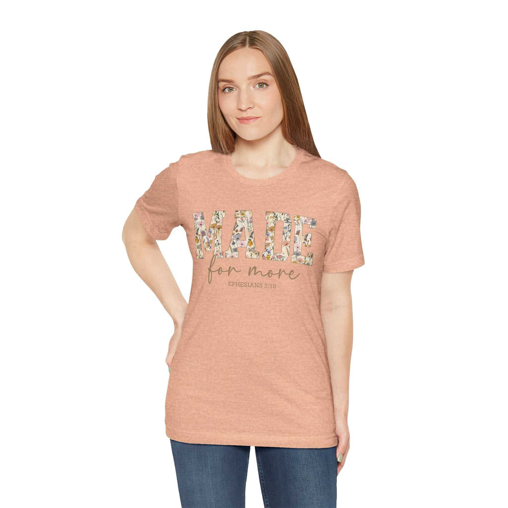 Woman wearing a Made for More Tee in light brown with floral lettering on front, paired with blue jeans