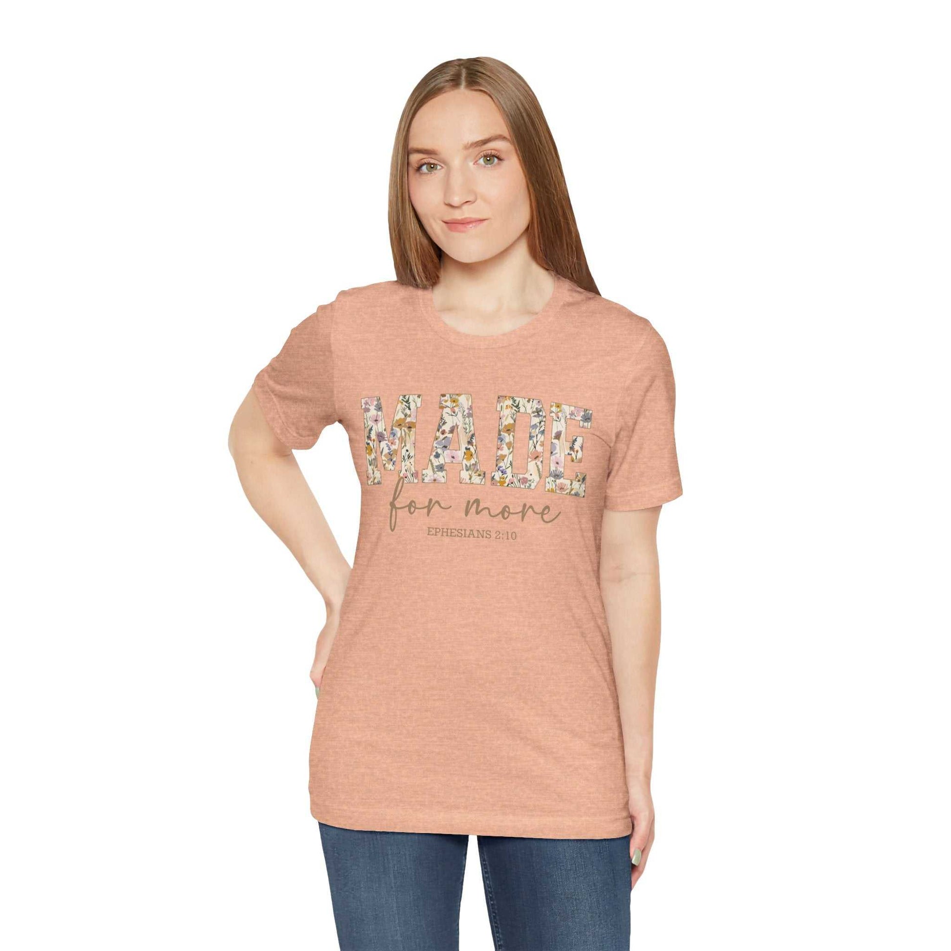 Woman wearing a Made for More Tee in light brown with floral lettering on front, paired with blue jeans